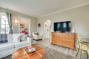 A living room with a white sofa, a coffee table with flowers, a wooden cabinet, and a flat-screen TV. - Family Apartment w/ Deck + Yard Near Northwestern (Evanston)