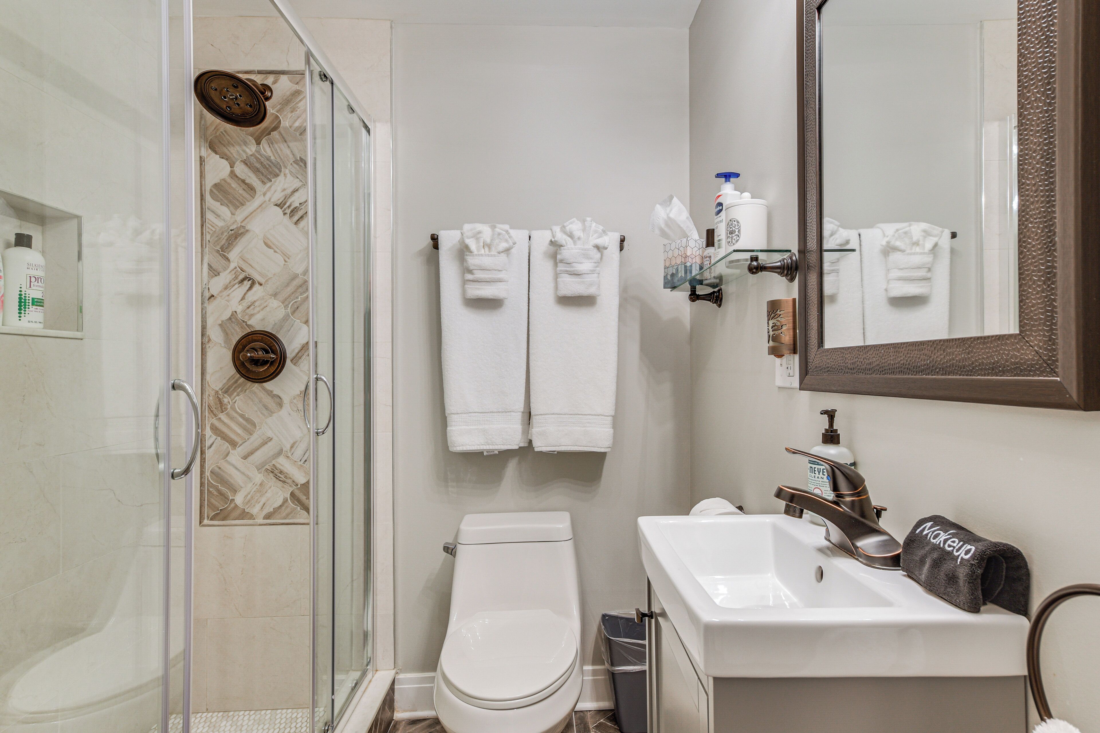 A modern bathroom with a glass shower enclosure, a white toilet, a sink with a mirror, and neatly hung towels.