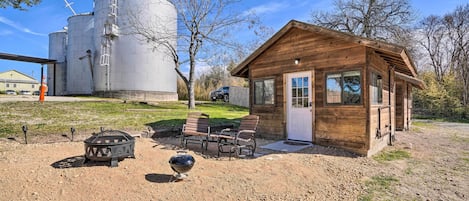 Una cabaña rústica con fachada de madera, un pequeño porche y un patio de grava con mobiliario exterior.