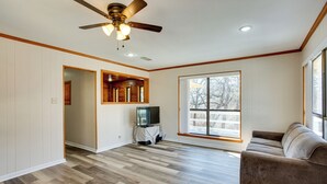 Un salon spacieux doté d’un plancher en bois, d’un ventilateur de plafond, d’une grande fenêtre et d’un canapé marron.