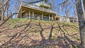 A two-story house with a wooden deck and a balcony, surrounded by trees and a grassy hill. - Lakefront Table Rock Getaway w/ Private Swim Dock! (Golden)