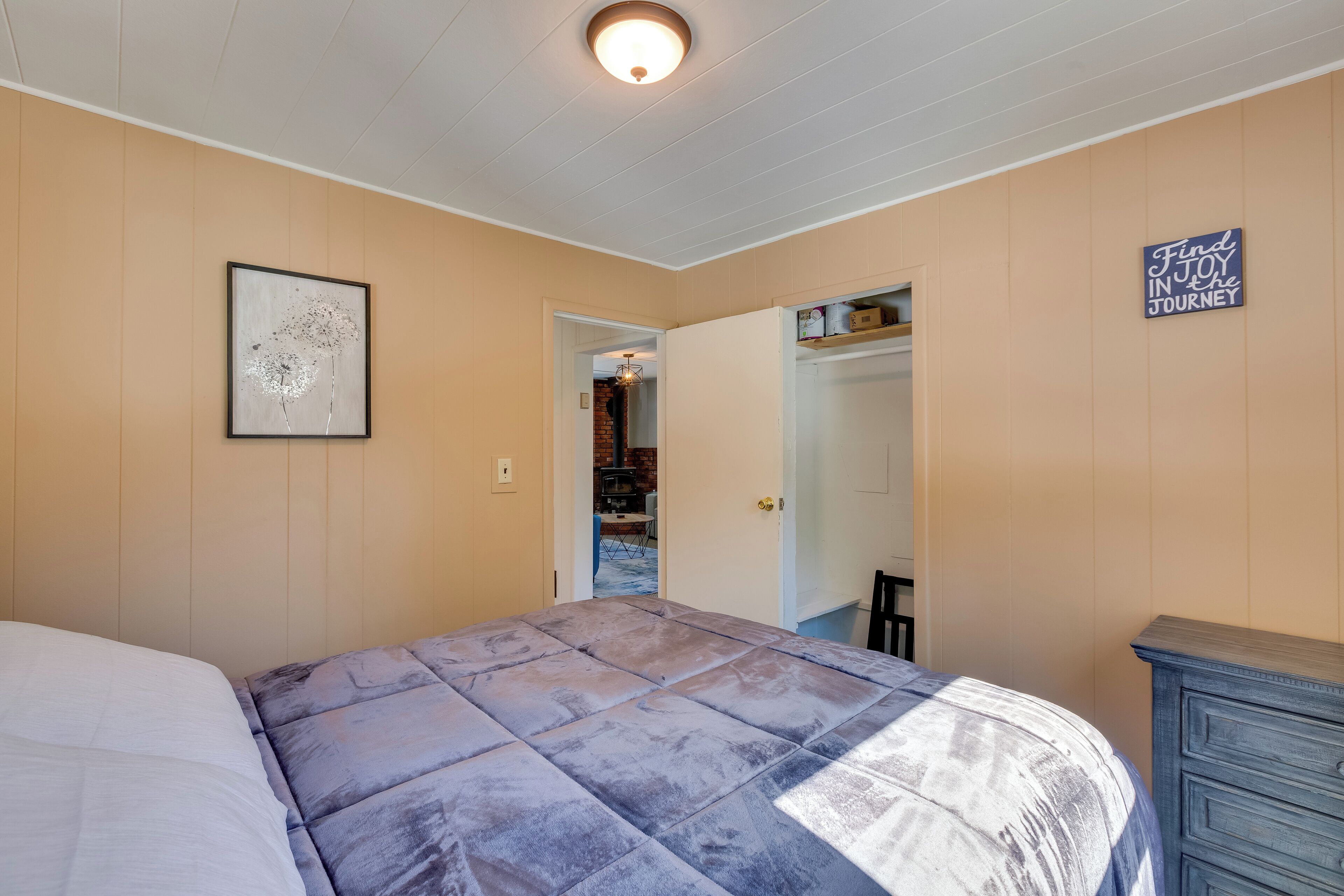 A bedroom with a bed, a dresser, a framed picture, and a sign on the wall.