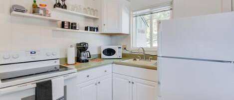 A compact kitchen with white cabinets, a microwave, a coffee maker, and a refrigerator.