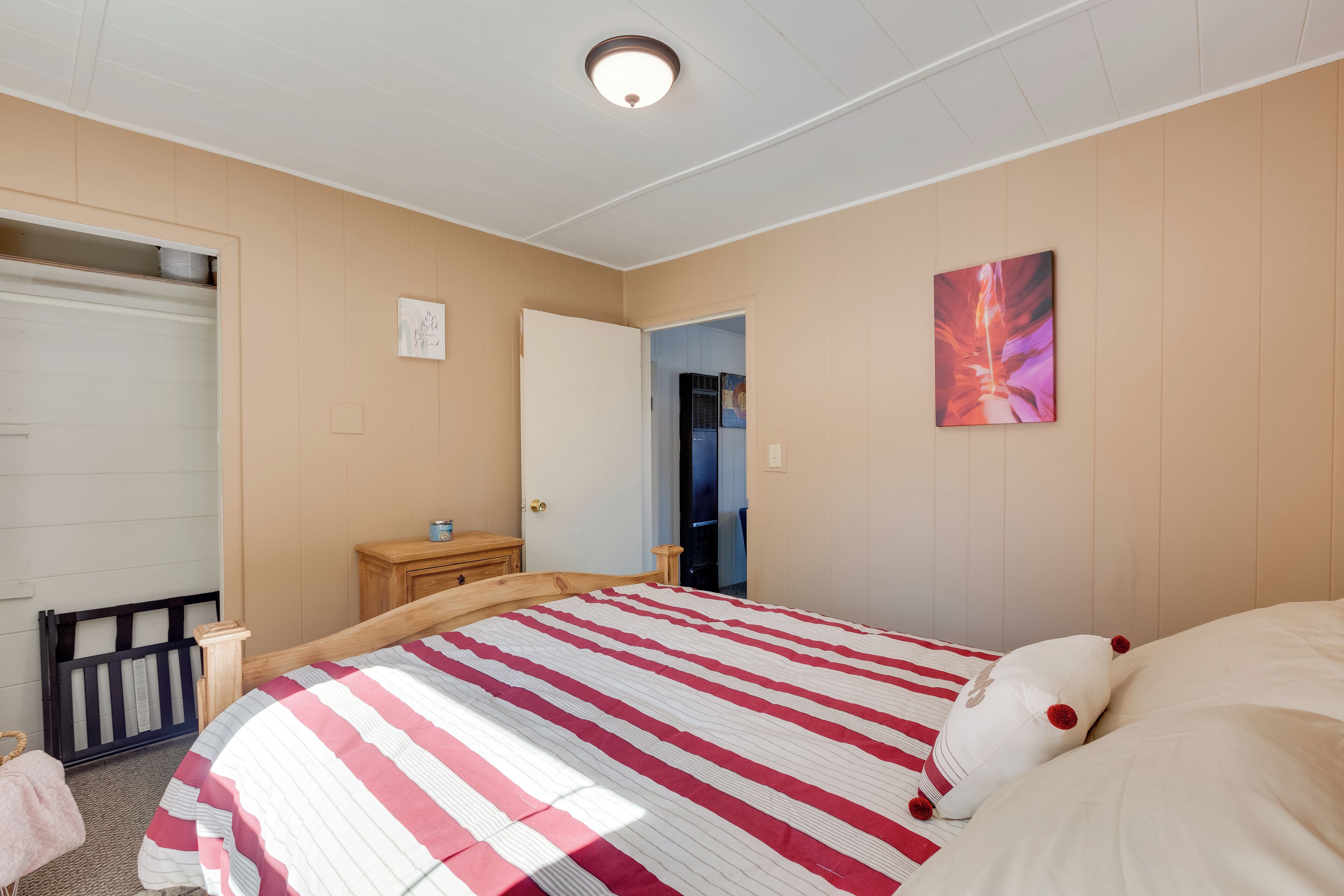 A bedroom with a bed, a dresser, a door, and a wall with a painting.