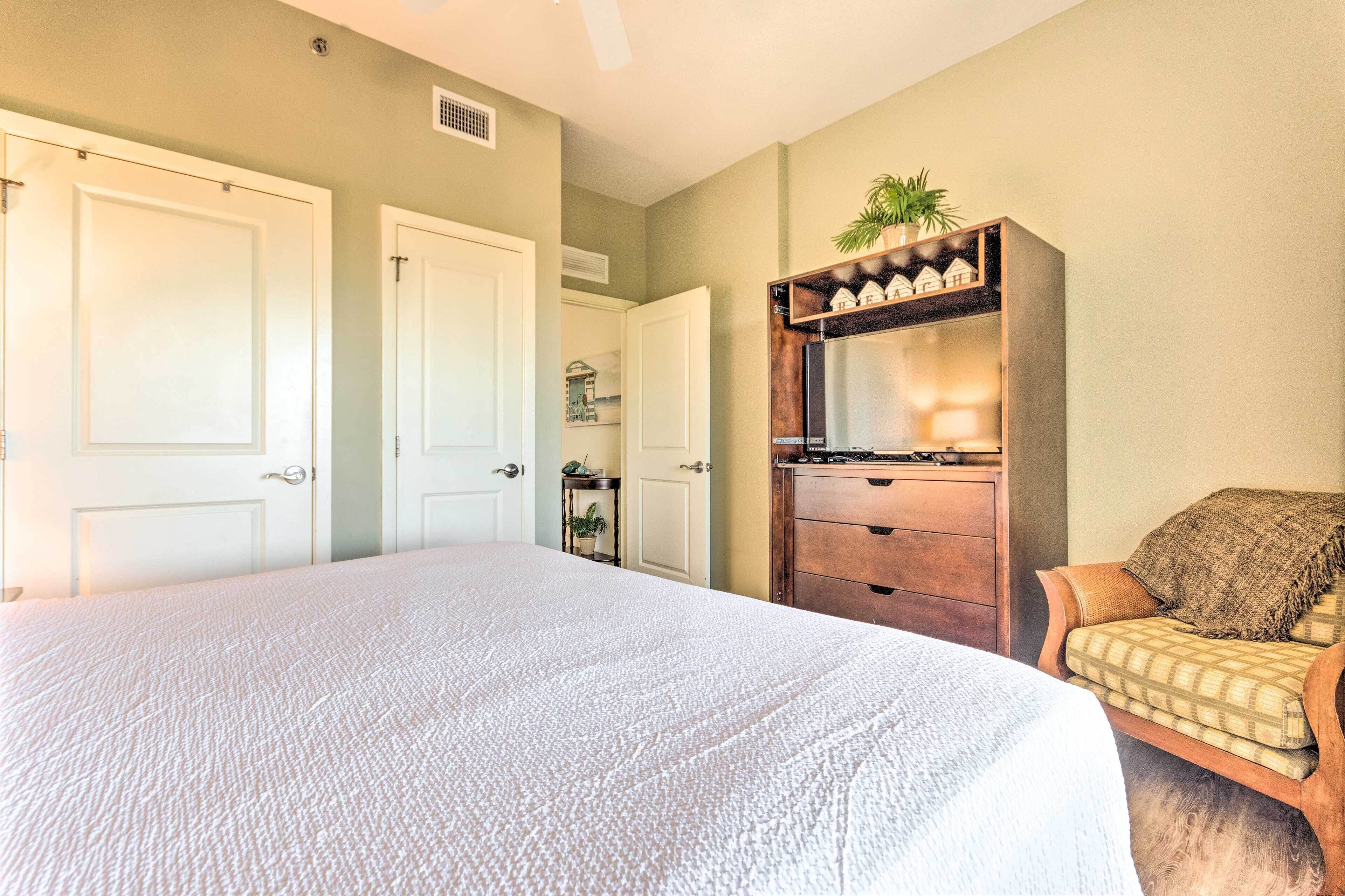 Une chambre à coucher avec un grand lit, une commode en bois, une chaise et une étagère ornée d’objets décoratifs.