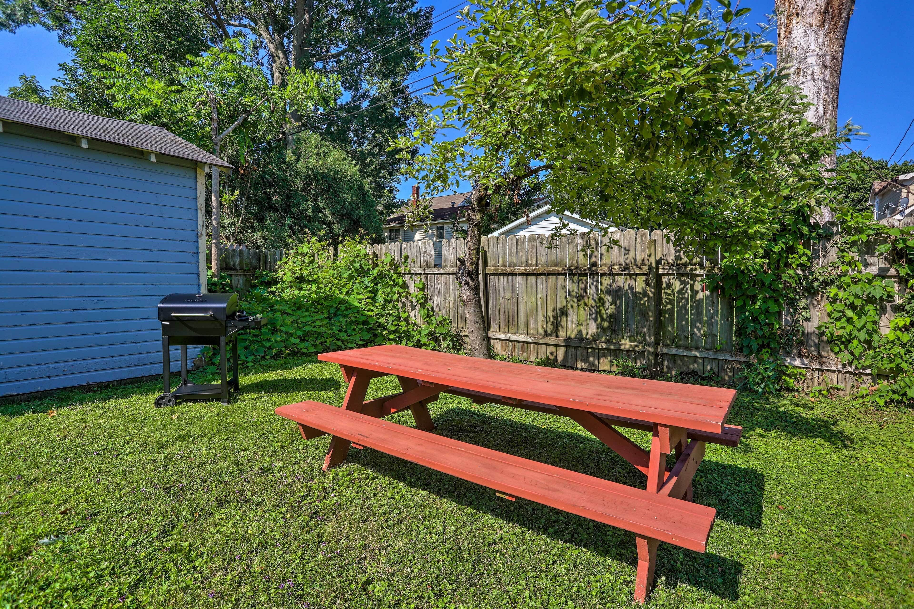 A red picnic table in a backyard with a blue shed and a wooden fence.