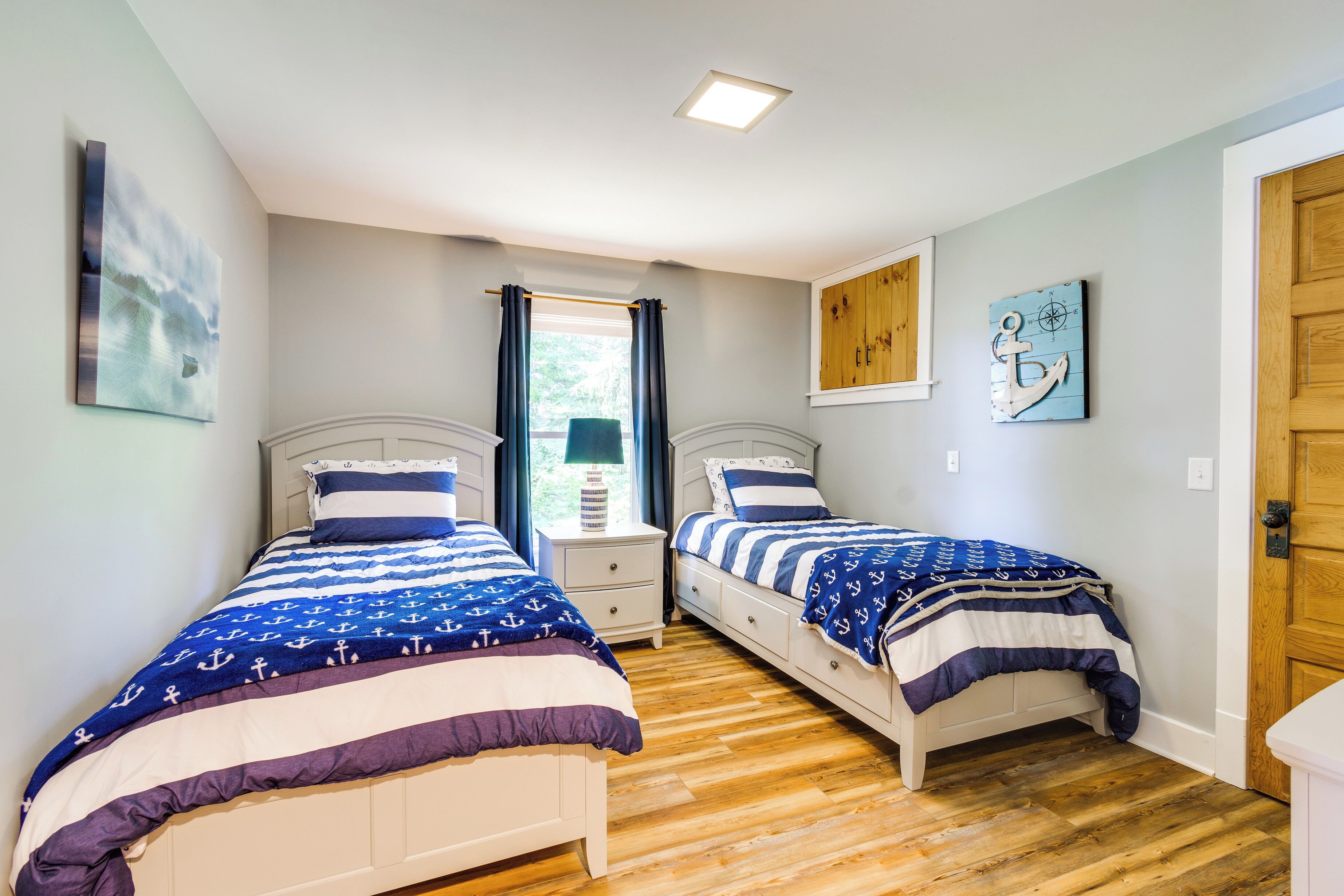 A bedroom with two beds, wooden flooring, and nautical-themed bedding.