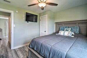 A bedroom with a bed, a ceiling fan, a TV mounted on the wall, and a door leading to another room. - Gulf Shores Condo - Walk to Beach & Restaurants! (Gulf Shores)
