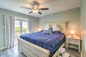 A bedroom with a bed, a nightstand, a ceiling fan, and a view of the outdoors. - Gulf Shores Condo - Walk to Beach & Restaurants! (Gulf Shores)