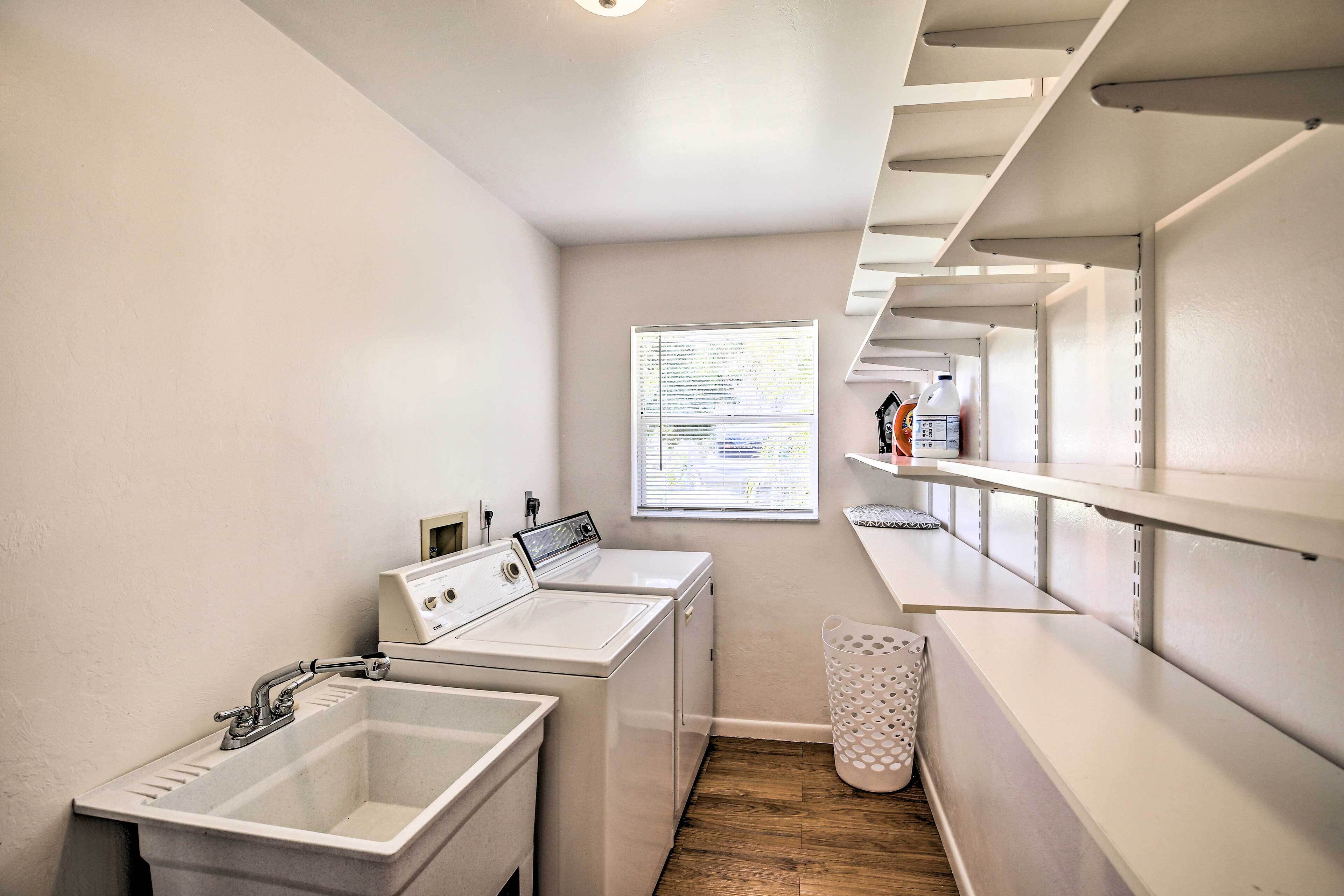 A laundry area with two washing machines, a sink, and a window with blinds.