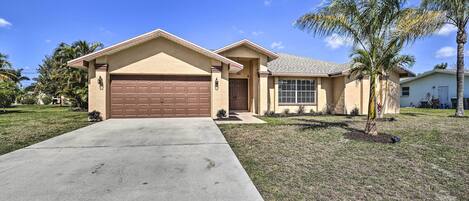 A single-story house with a brown garage, a front entrance, and a small front yard with a palm tree.