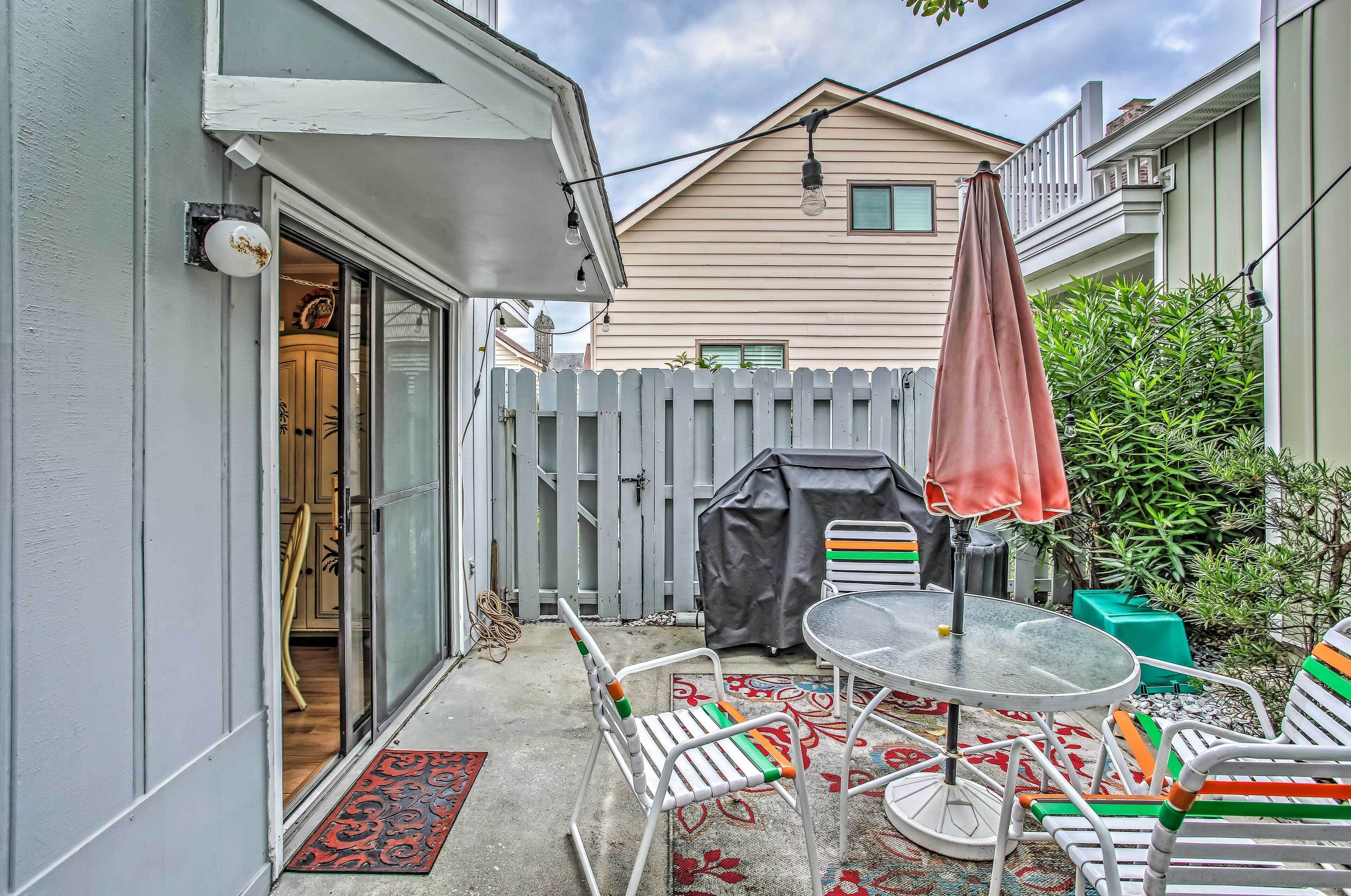 A patio with a table and chairs, a covered grill, and a white picket fence.