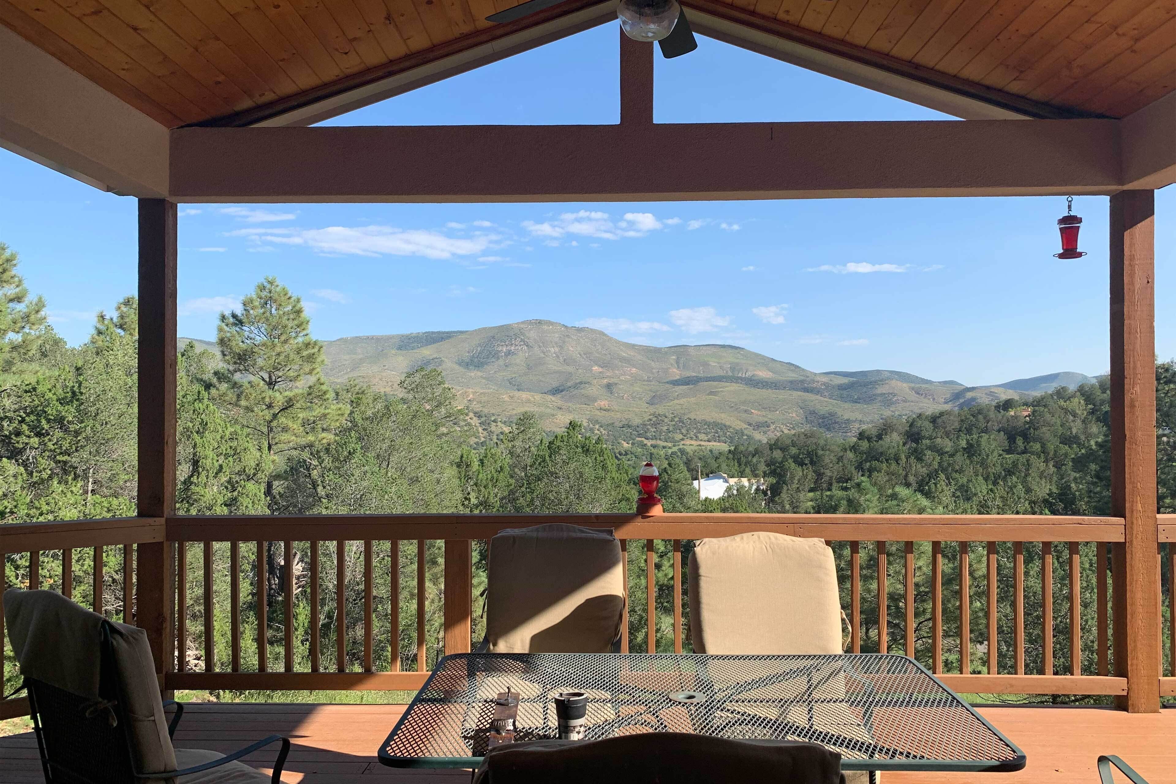 Uma área de estar coberta ao ar livre, com uma mesa e cadeiras, com vista para uma paisagem montanhosa.