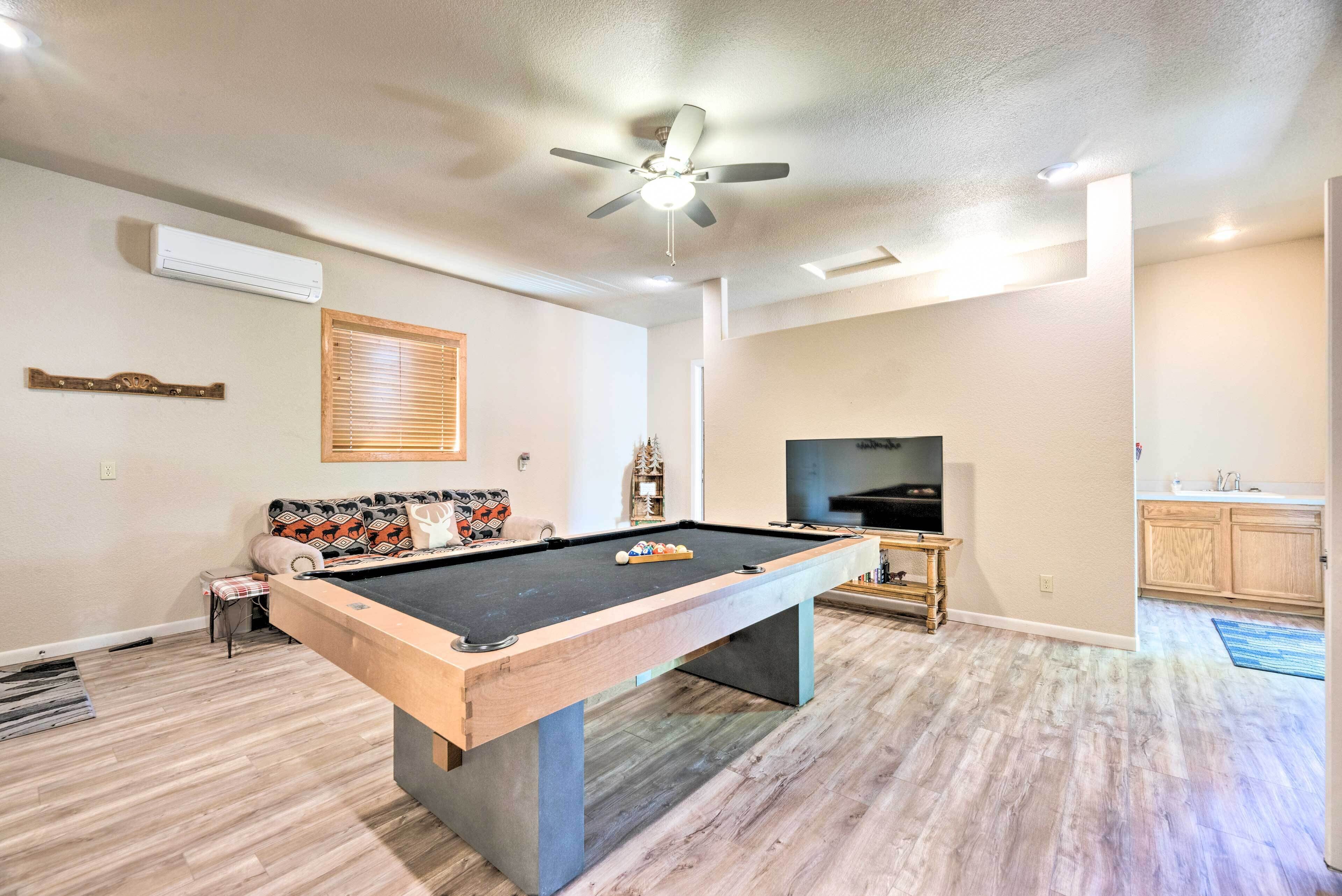 A pool table in a living room with a ceiling fan, a television, and a sofa.