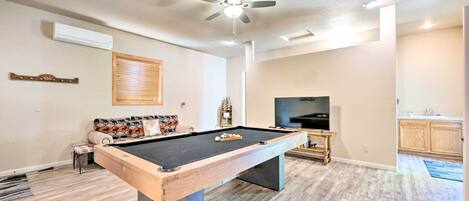 A pool table in a living room with a ceiling fan, a television, and a sofa.