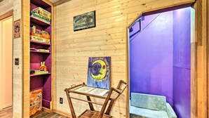 A room with wooden walls, a purple wall, a wooden chair, a table with papers, and shelves with board games.