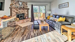 A living room with a fireplace, a leather sofa, a wooden coffee table, and a balcony with a view of trees.