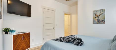 A bedroom with a bed, a TV mounted on the wall, a wooden cabinet, and a door leading to another room.