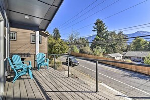 A wooden deck with two blue Adirondack chairs, a covered area, and a view of a road and mountains.