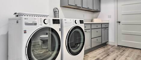 A laundry room with two white LG front-loading washing machines, grey cabinets, and a white door.