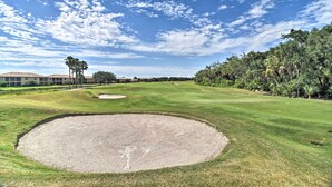 Golfkenttä, jossa on suuri hiekkabunkkeri, hyvin hoidettu nurmikko ja kirkas, sininen taivas.