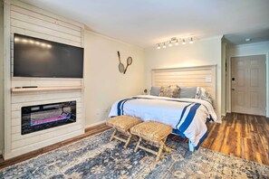 A bedroom with a large bed, a television mounted on a wooden panel wall, a fireplace, and a patterned rug. - Balcony + Pool Access! Couples Escape in Lake Lure (Lake Lure)