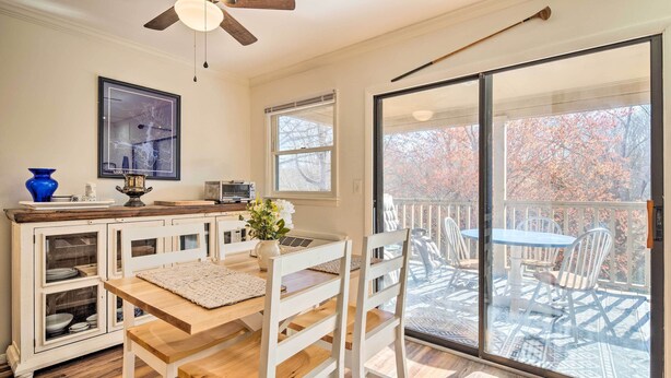 A dining area with a wooden table and white chairs, a white cabinet with glass doors, and a view of a balcony with outdoor furniture. - Balcony + Pool Access! Couples Escape in Lake Lure (Lake Lure)