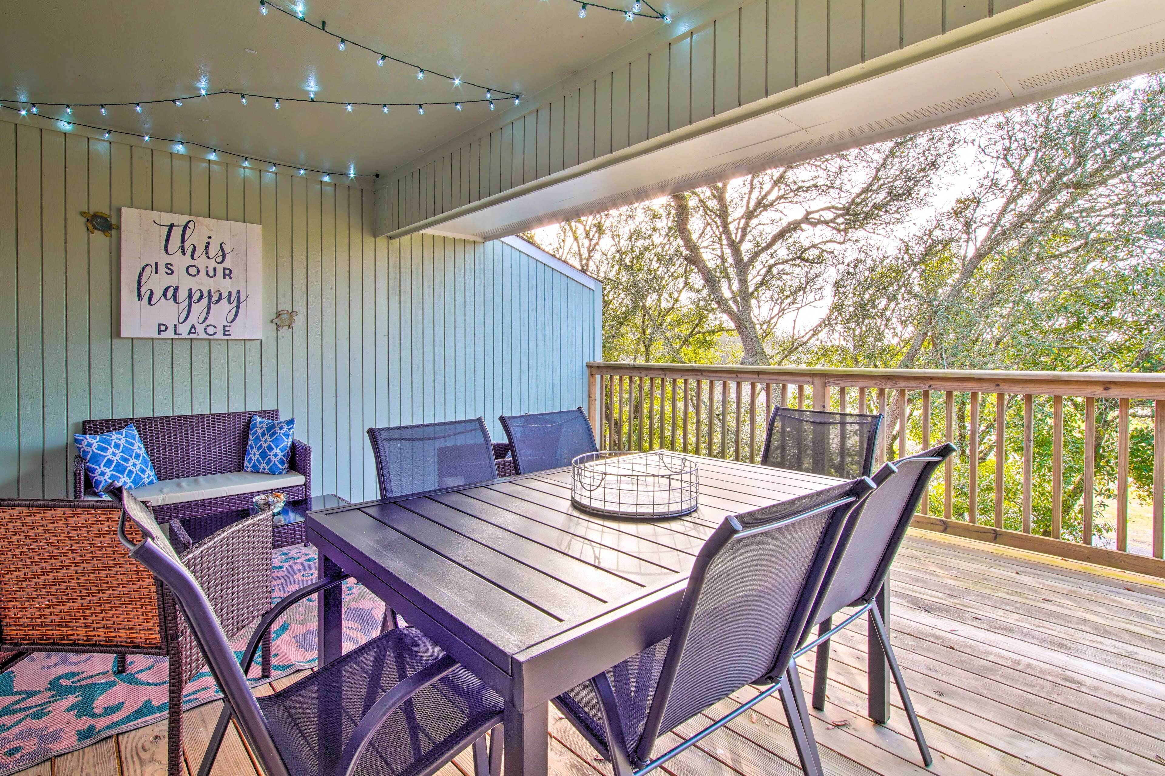 A covered patio with a table and chairs, a wicker sofa, and a sign that says "this is our happy place."
