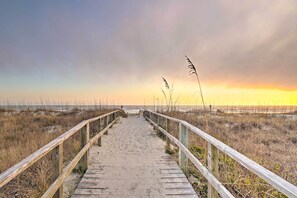 Une promenade en bois menant à une plage, avec un coucher de soleil en arrière-plan.
