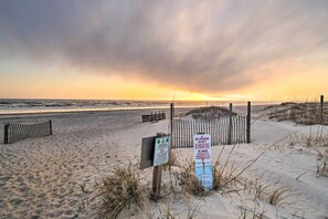 A beach with a wooden fence, warning signs, and a sunset in the background.