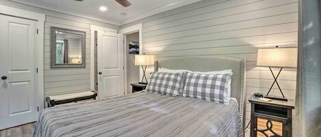 A bedroom with a large bed, two bedside tables with lamps, a ceiling fan, and a door with a mirror.