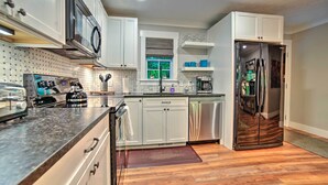 A modern kitchen with white cabinets, stainless steel appliances, and a wooden floor.