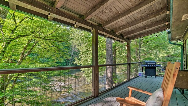 A covered deck with a view of a forest and a stream.
