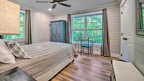 A bedroom with a bed, a ceiling fan, a window with curtains, and a view of greenery outside.