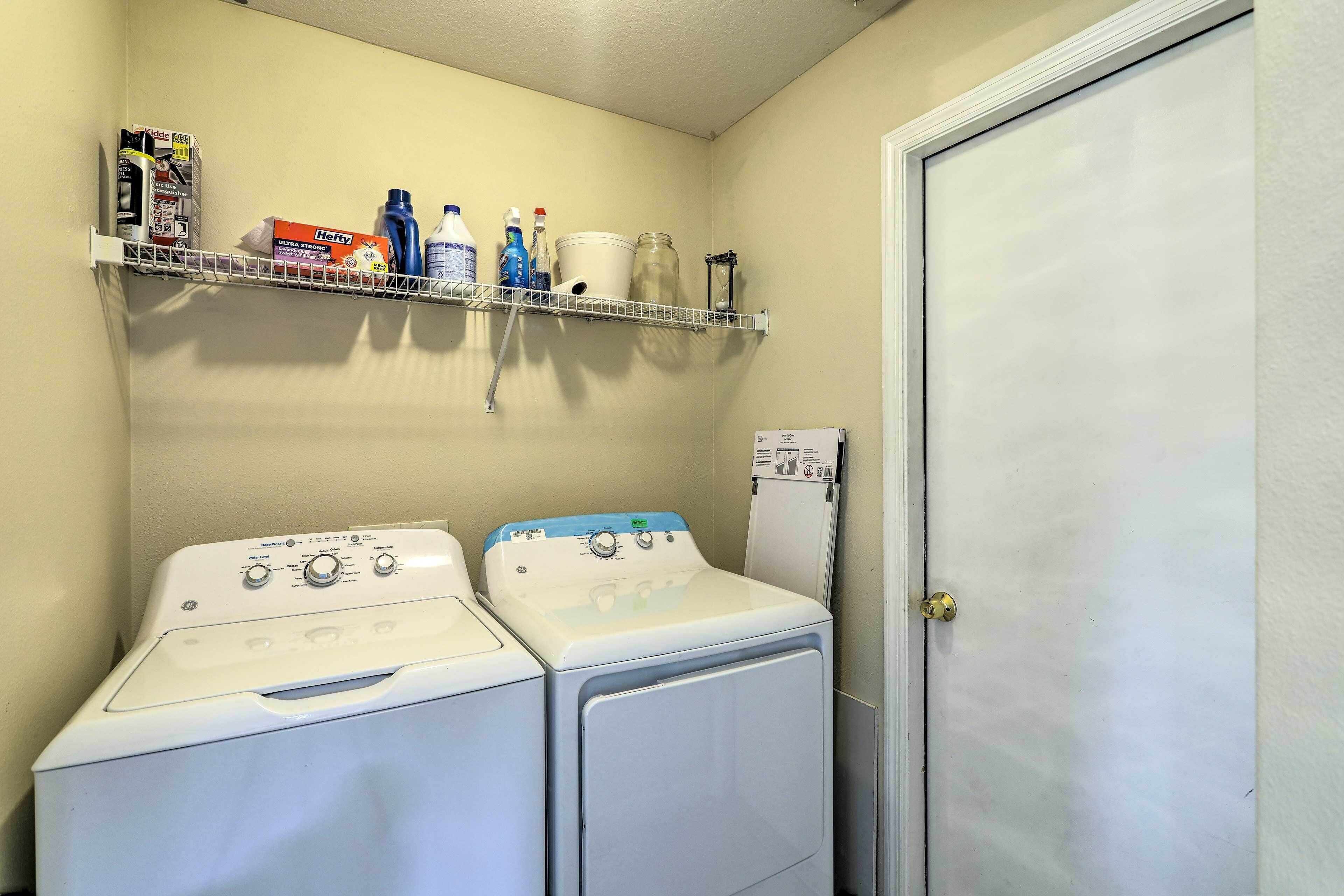 A laundry area with two front-loading washing machines and a shelf above holding cleaning supplies.