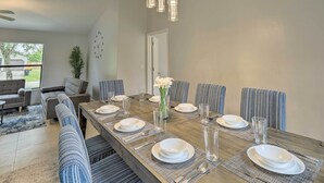A dining room with a long table set for six, surrounded by striped chairs, a sofa, and a potted plant. - Charming Palm Bay Retreat w/ Spacious Yard! (Palm Bay)