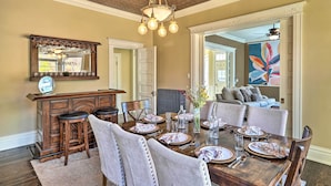 Un espace repas avec une table en bois dressée pour six personnes, entourée de chaises rembourrées. Un coin bar avec des tabourets est visible sur la gauche.