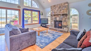 A spacious living room with a stone fireplace, large windows, and a cozy seating area. - Near Hiking: Lakefront Albrightsville Home w/ Deck (Albrightsville)