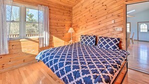 A wooden-paneled bedroom with a bed, a lamp, and a view through a window. - Near Hiking: Lakefront Albrightsville Home w/ Deck (Albrightsville)