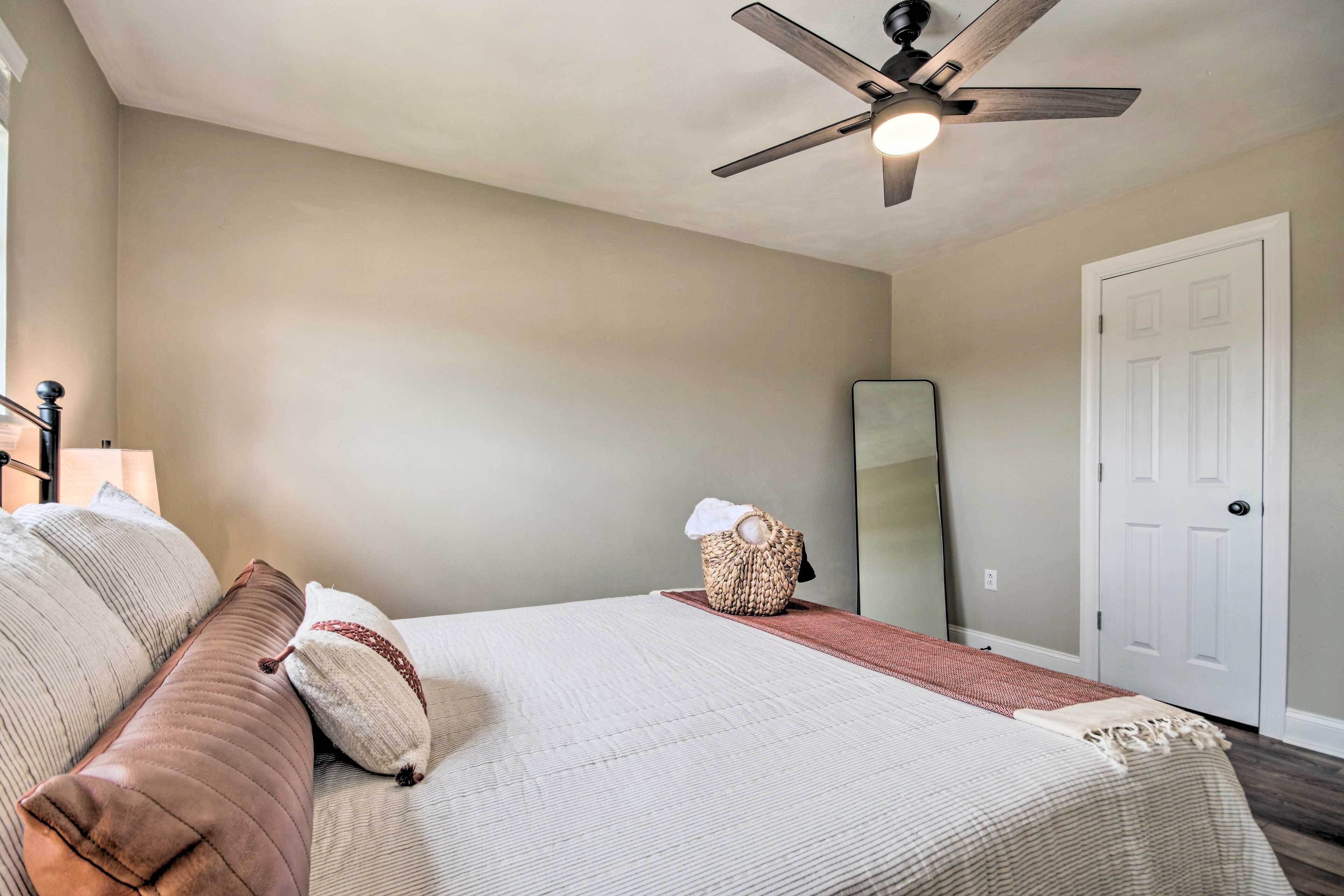 A bedroom with a bed, a ceiling fan, a mirror, and a door.