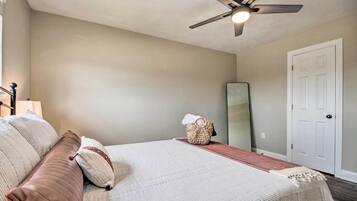 A bedroom with a bed, a ceiling fan, a mirror, and a door.