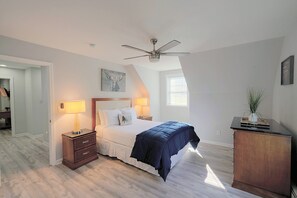 Un dormitorio con cama, lámparas de noche, ventilador de techo, un cuadro y una ventana con persianas.