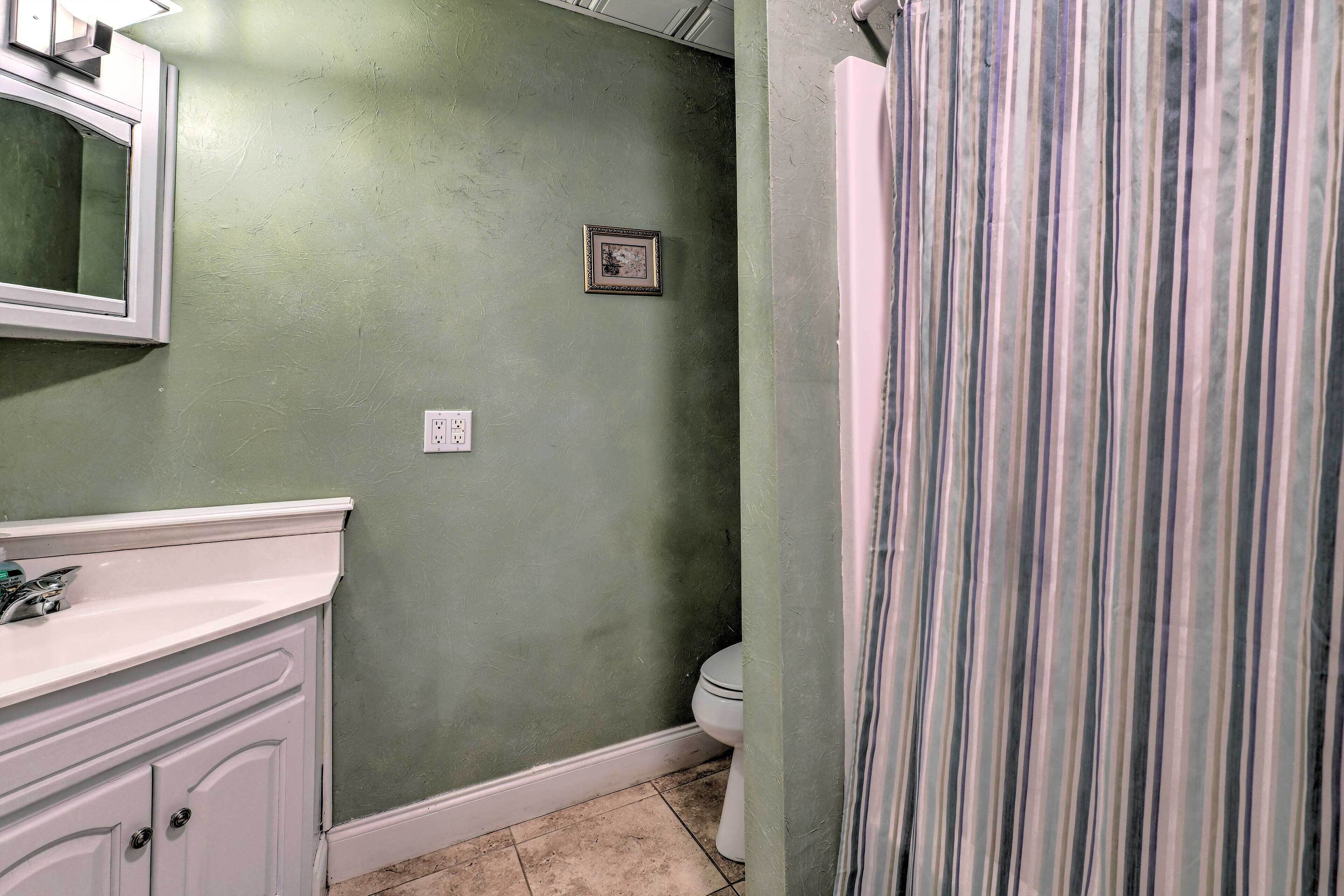 A bathroom with a green wall, a white sink, a framed picture, and a striped shower curtain.