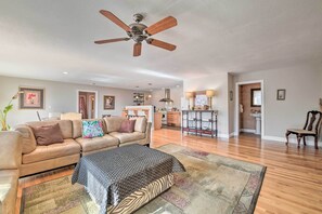 Un salon spacieux avec un canapé beige, un tapis à motifs et un ventilateur de plafond.