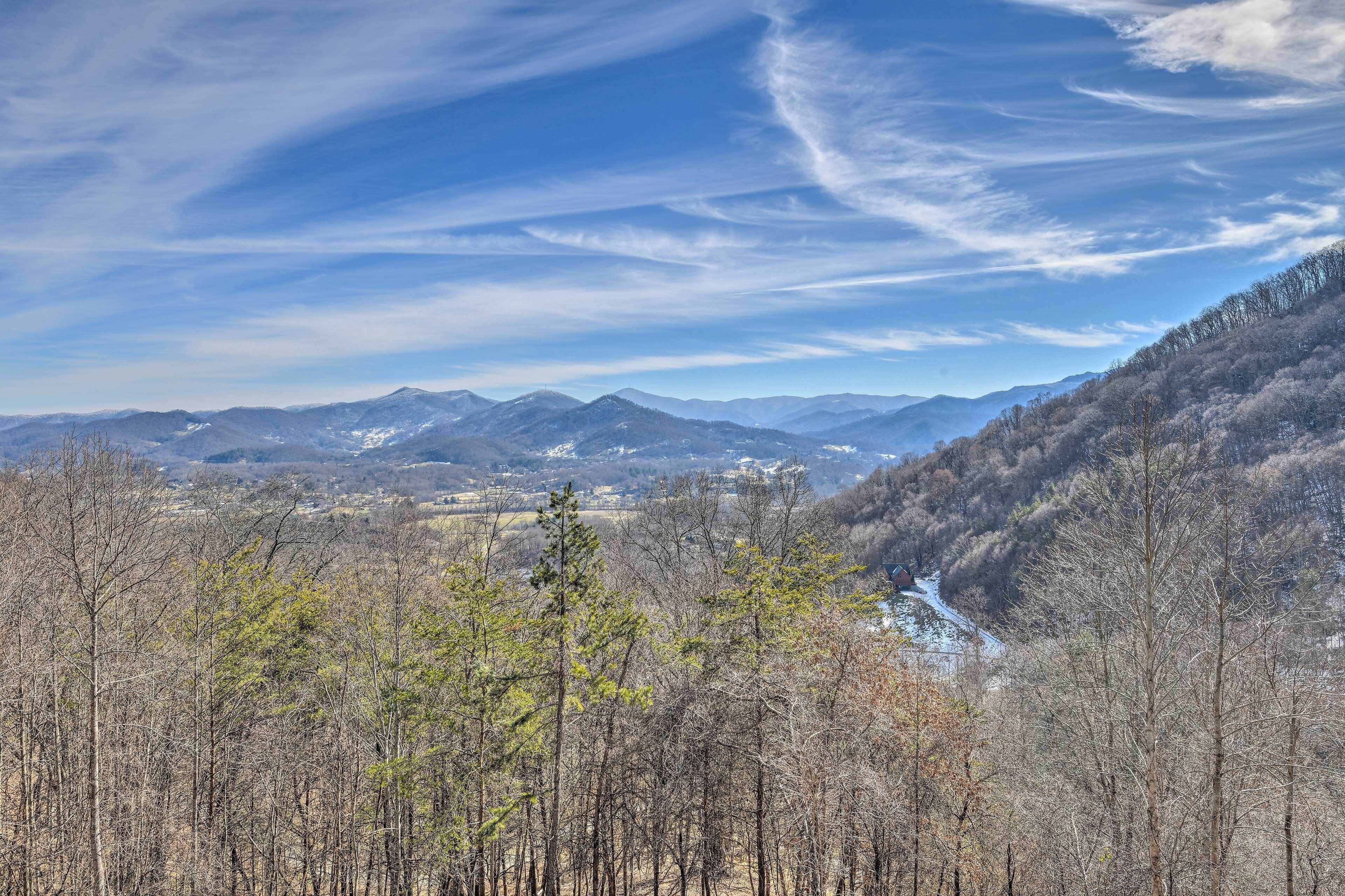 A mountainous landscape with a river, dense forest, and distant mountains under a clear sky.