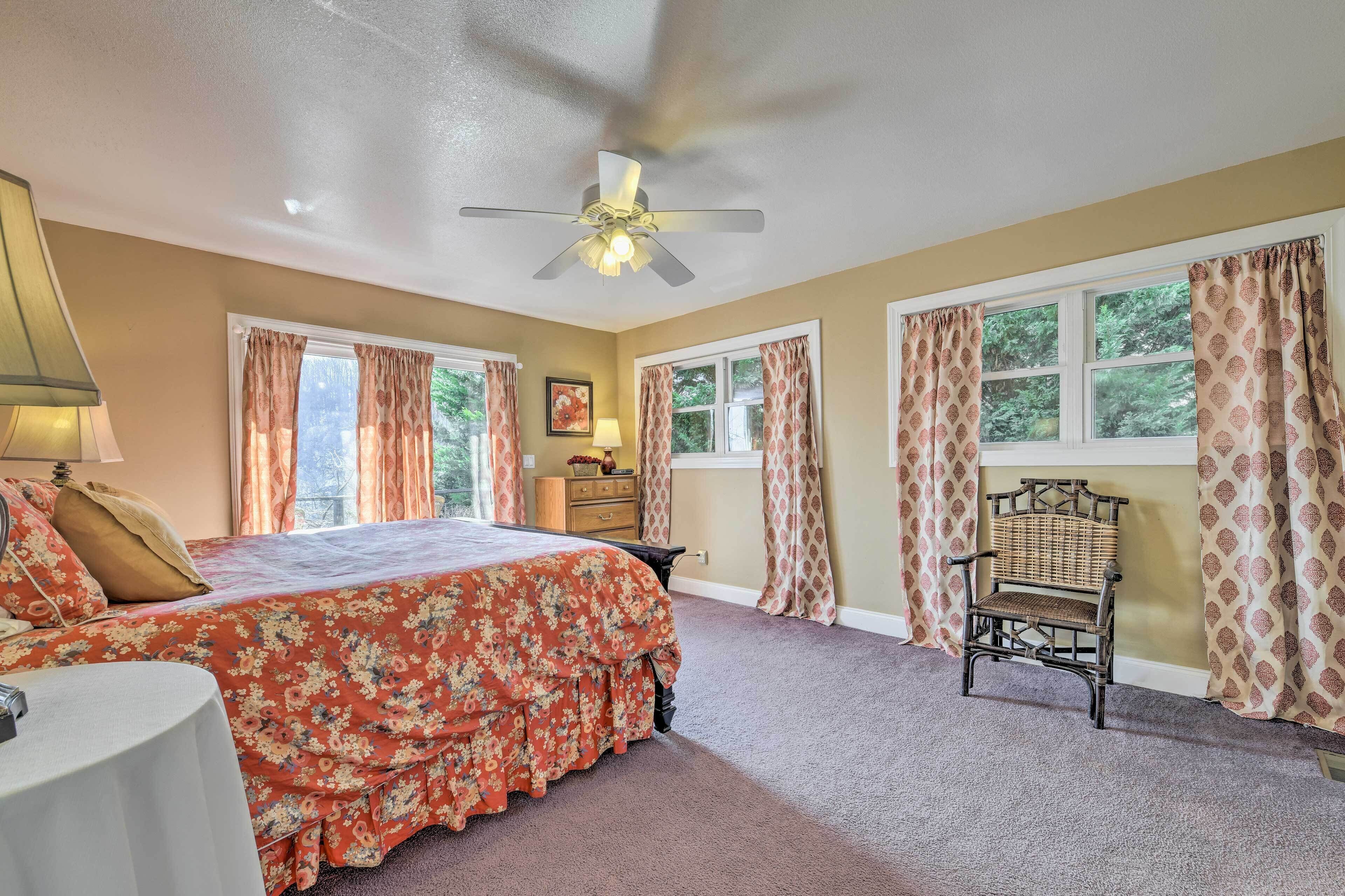 A bedroom with a bed, a chair, a ceiling fan, and two windows with curtains.