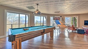 Een ruime kamer met een pooltafel, grote ramen en een hangmat.