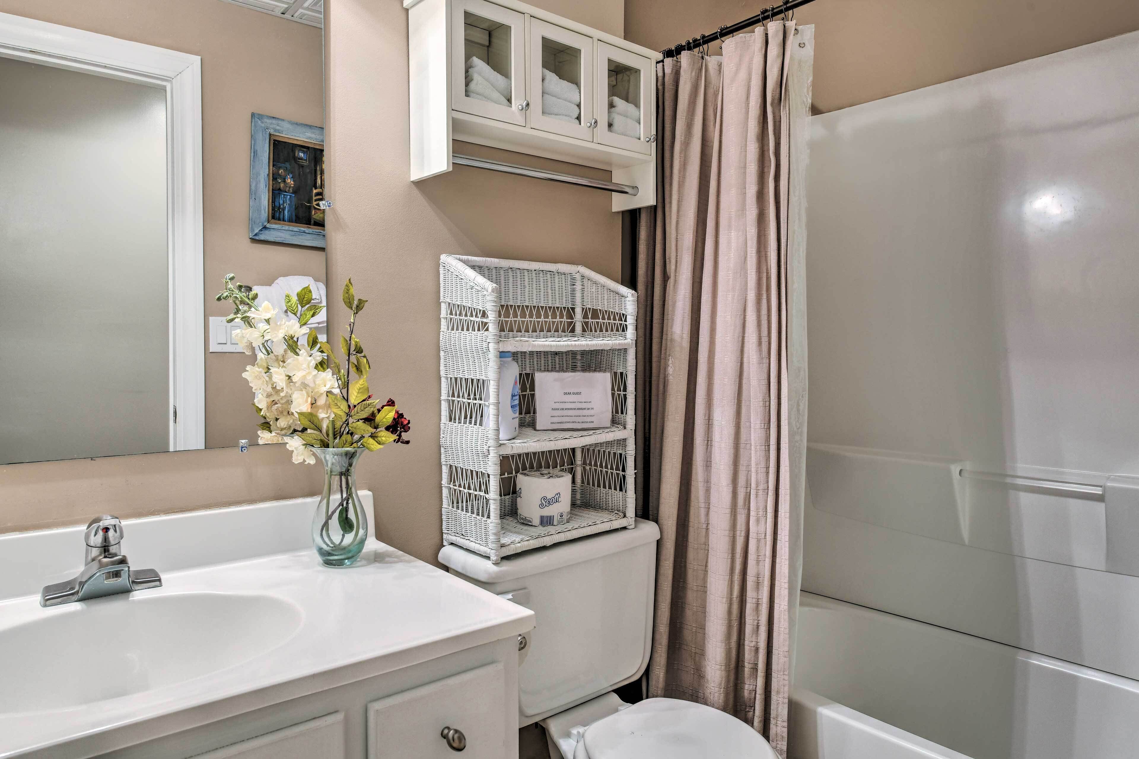 A bathroom with a white sink, a mirror, a toilet, a shower, and a wicker shelf with toiletries.