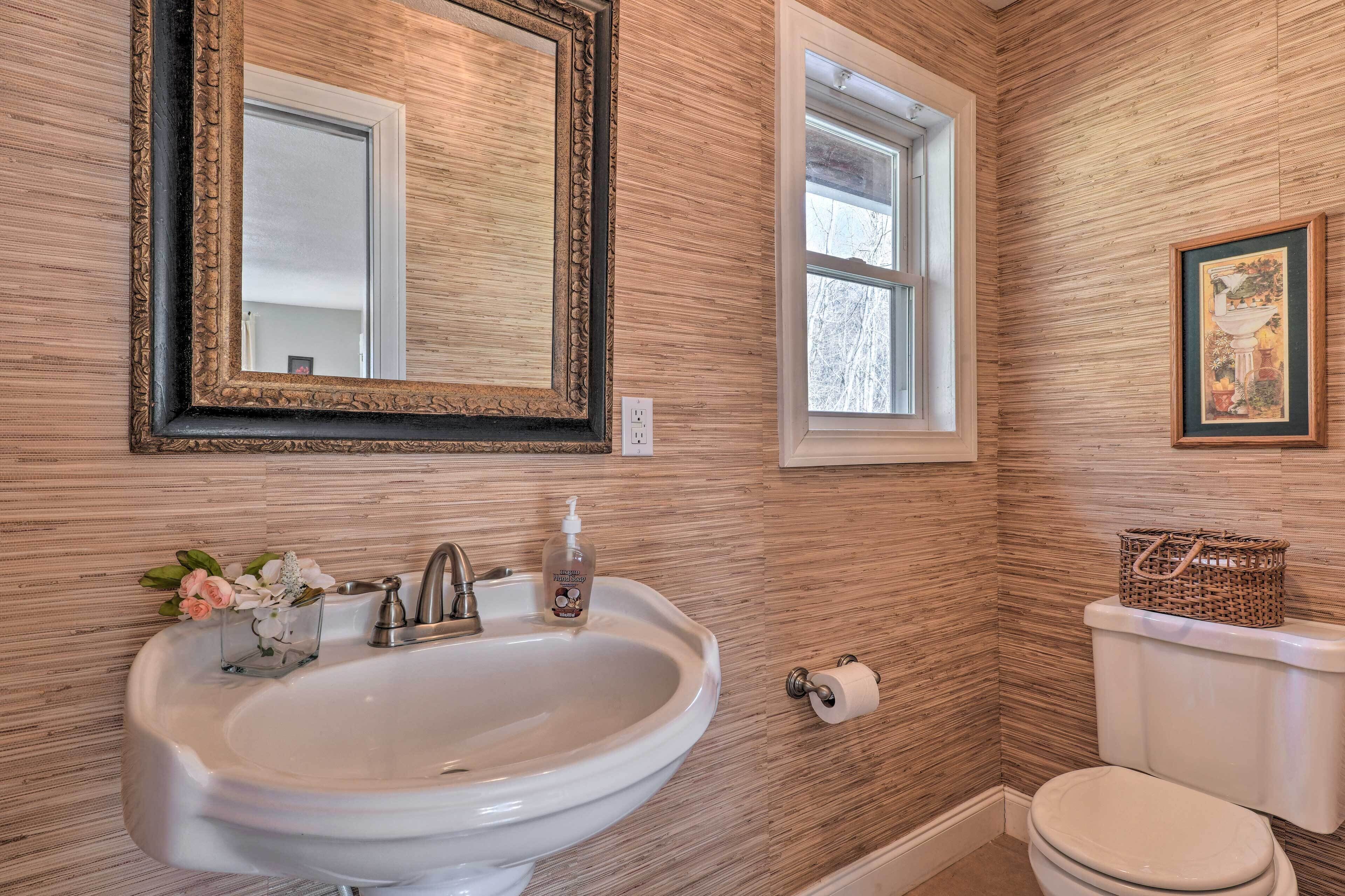 A bathroom with a wooden wall, a white sink, a mirror, a window, and a toilet.
