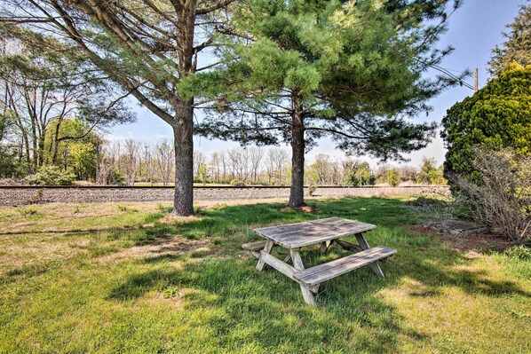 A picnic table in a grassy area with trees and a stone wall in the background.